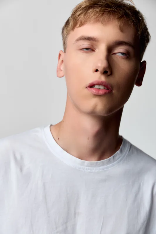 Closeup, male, young, face, expression, casual, shirt, fashion in a studio with soft lighting highlighting skin texture and a relaxed gaze for contemporary editorial appeal