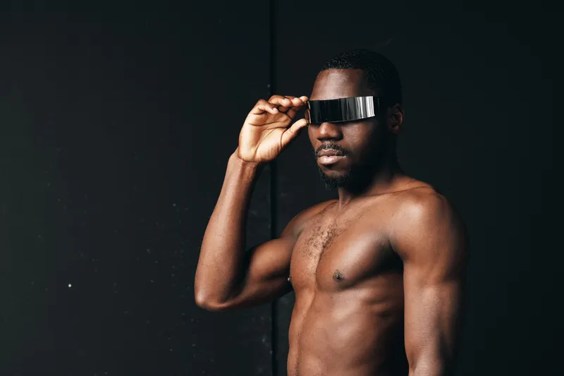 African man with dark skin and muscular body wearing futuristic visor in creative conceptual visual style on black background. Portrait of confident male model with modern accessory.
