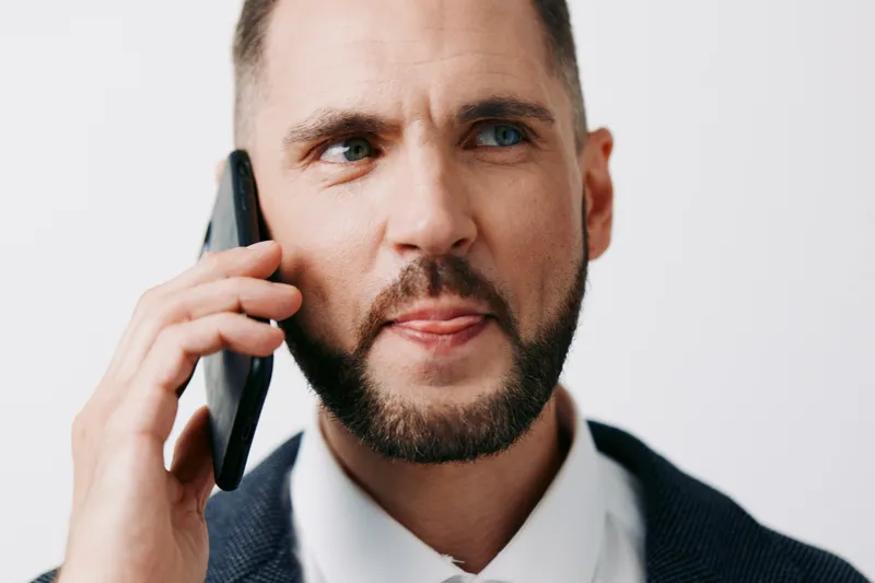A focused business professional man speaks on a mobile phone, presenting confidence and concentration. The isolated colored background emphasizes the moment and intent.