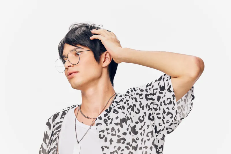 young man with glasses wearing leopard print shirt posing thoughtfully against white background with casual hairstyle and silver chain, stylish and modern look