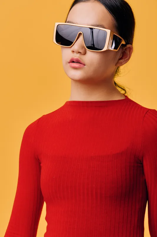 Woman with sunglasses and red sweater posing in studio on yellow background. Fashionable female model wearing trendy eyewear and elegant casual outfit with neutral expression.