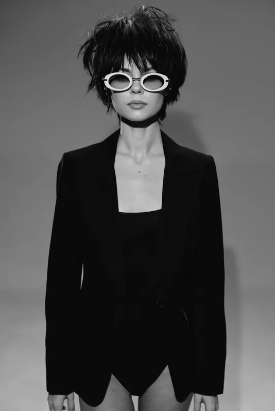 Black and white portrait of a woman with short hair wearing sunglasses and a black blazer.