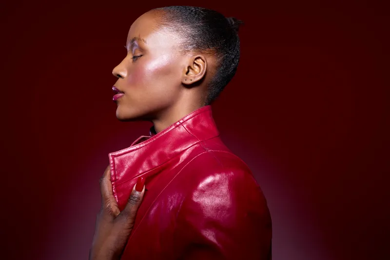 Profile of an elegant dark skinned African woman with shiny skin wearing a red leather jacket on red background. Concept of fashion, beauty, style, and confident female model.