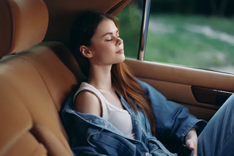 Young woman in casual denim outfit relaxing in a car, conveying tranquility and freedom, green background highlighting a serene, seasonal vibe.