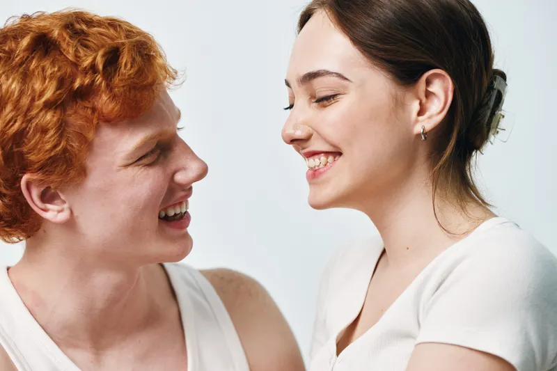 Young couple smiling and looking at each other, happy and joyful emotions in casual white clothes. Relationship, love and interaction with bright background and natural light.