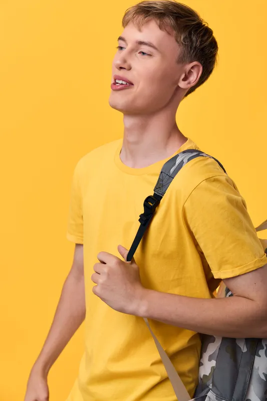 Young student with a backpack on a bright yellow backdrop, casual exploration vibe, campus energy, learning mood, sunny movement, curiosity and adventure in motion