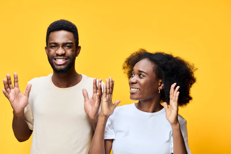 Happy young African American couple celebrating with joy against a bright yellow background, expressing excitement in casual attire with playful emotions