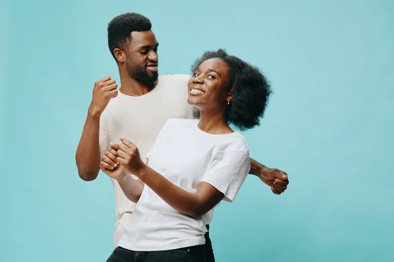 Happy young couple dancing together, showcasing joy and connection against a light blue background, representing love and togetherness, perfect for lifestyle themes