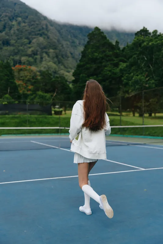 Young woman in a casual outfit walks on a tennis court, showcasing confidence and joy amidst a lush green mountain backdrop, perfect for sports and outdoor themes