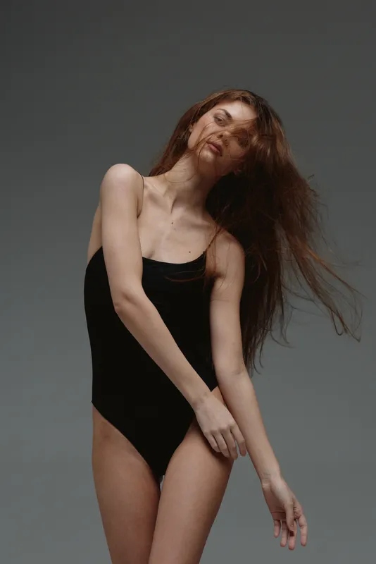 young woman posing with flowing hair in black bodysuit, studio background, graceful and natural mood