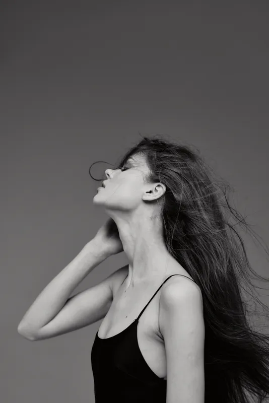 Black and white profile portrait of a young woman with flowing hair in a simple black top, showcasing elegance and calm emotion.