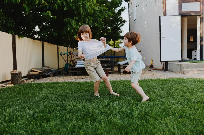 Happy children playing outdoors, enjoying a sunny day in a lush green yard, showcasing joy and friendship while running together.