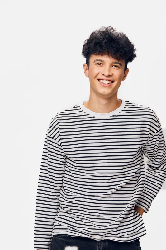 smiling young man wearing a striped long sleeve shirt standing against a white background, casual style, cheerful expression