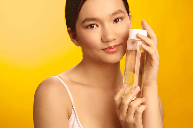 asian woman with dark hair wearing a light top holds a transparent bottle against a bright yellow backdrop, creating a fresh lifestyle moment focused on hydration and wellness.