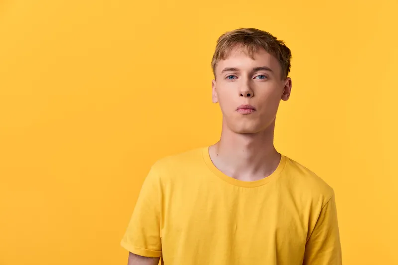 Minimalist image of a young man in a bright yellow shirt against a solid yellow backdrop, emphasizing color harmony, casual style, and contemporary fashion visual.