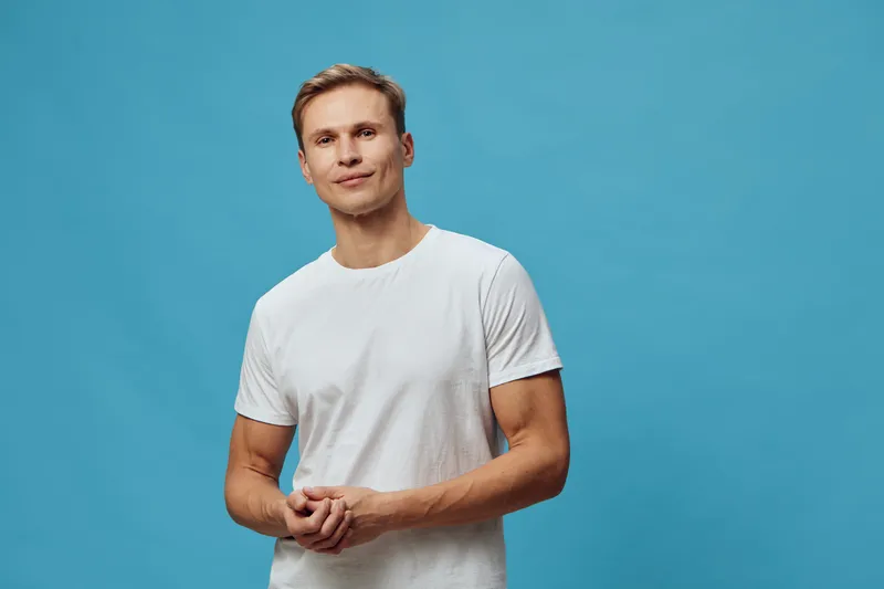 Smiling man with light brown hair wearing casual white t-shirt standing against a solid blue background. Studio portrait of a cheerful adult male. People lifestyle concept.