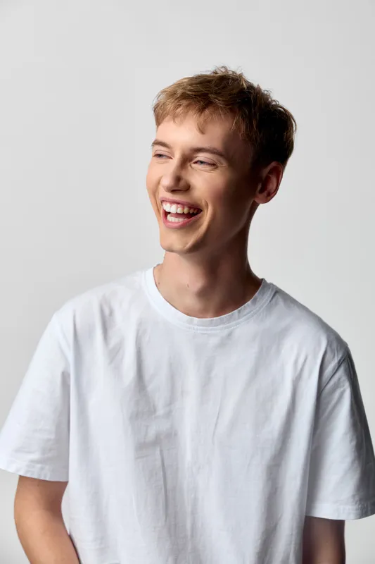 Smiling man in a casual white t shirt stands in a bright studio, conveying joy, friendly energy and an approachable vibe for lifestyle, fashion or wellness advertising campaigns