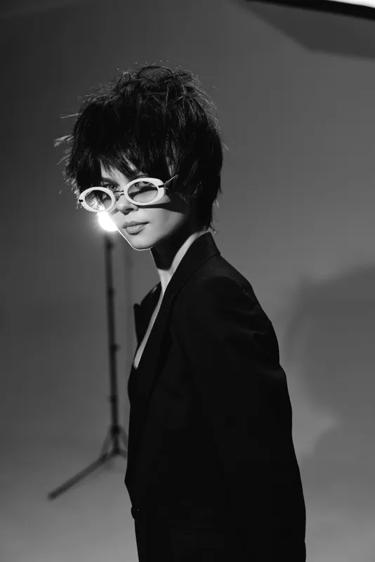 Black and white portrait of stylish woman with short hair and sunglasses posing in studio with soft lighting.