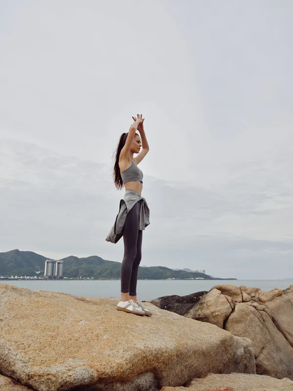 Athletic woman practicing yoga on rocky beach, enjoying tranquility of nature and fresh air, wearing sporty outfit and exuding positivity and mindfulness