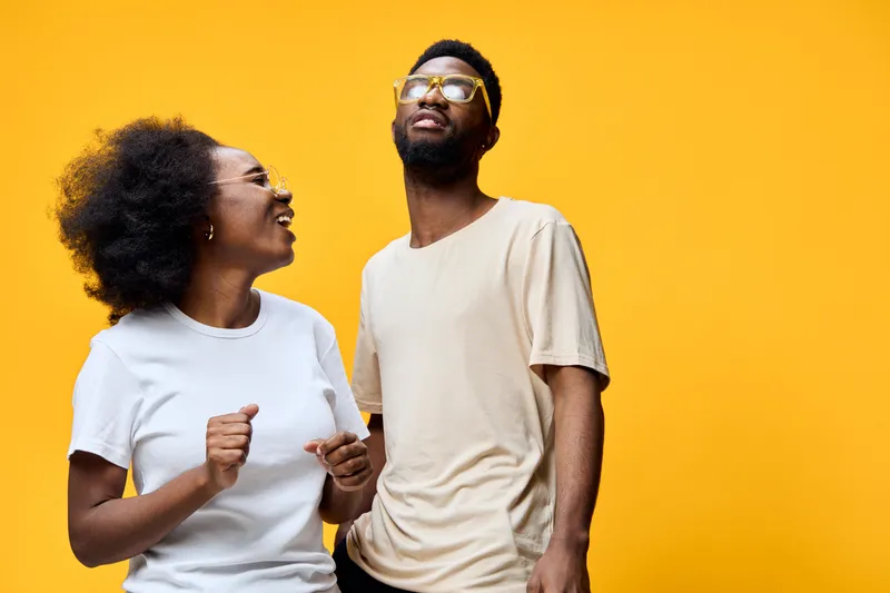 Happy African American couple laughing together against a bright yellow background, showcasing joy and connection through vibrant fashion and emotions