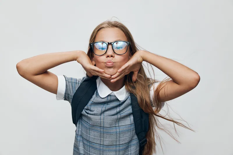 Girl child with glasses posing with hands near face smiling playful emotion with long hair wearing school uniform on white background portrait studio isolated.