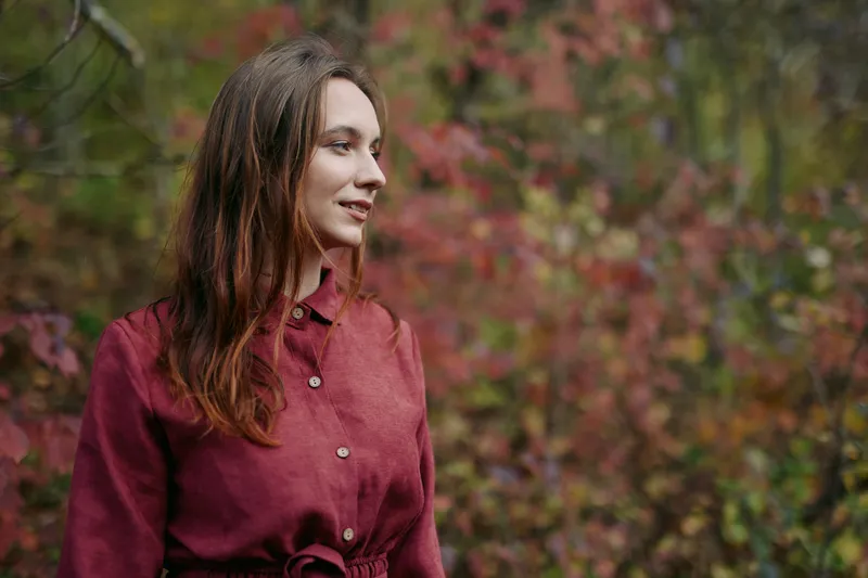 Portrait of a young woman in natural autumn surroundings, sincere expression and relaxed pose conveying authenticity and accurate skin tones captured in soft natural light.
