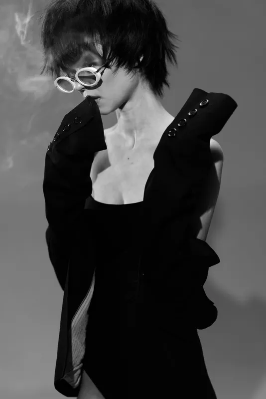 Black and white portrait of a stylish woman wearing sunglasses in a dark outfit, exuding a mysterious and edgy vibe.