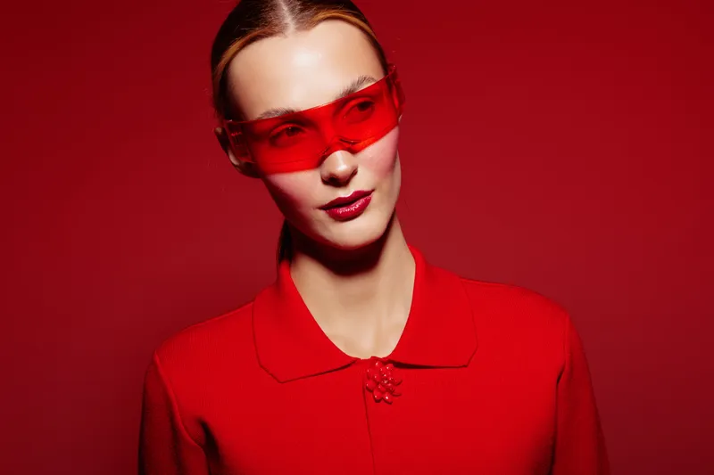 Stylish woman in red outfit and red sunglasses poses confidently against red background. Fashion portrait with bold colors and modern accessories for trendy style concept.