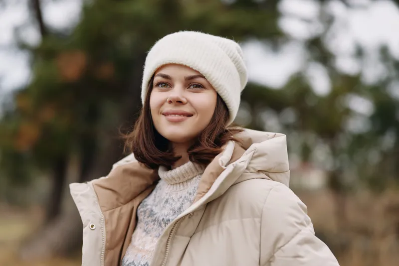 Winter, woman portrait outdoors in a warm coat and beanie, soft natural light, relaxed smile, autumn background. Casual fashion moment showcasing cozy seasonal style for lifestyle photography