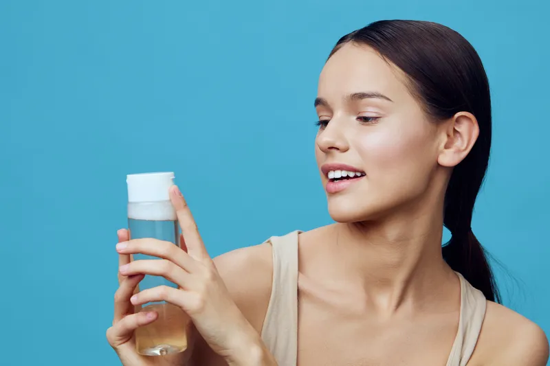 Young woman holding a skincare product, smiling joyfully against a blue background, highlighting beauty and self care in a vibrant and fresh style
