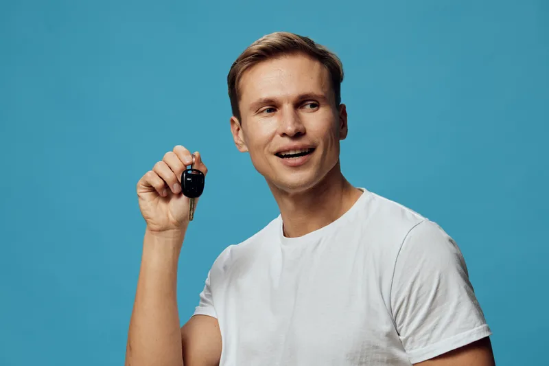 Smiling man hold car key look away wear white t-shirt isolated on blue background digital nomad freelance concept