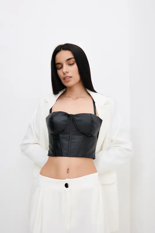 young woman wearing white suit and black leather bustier posing against white background with relaxed expression in minimalistic fashion portrait
