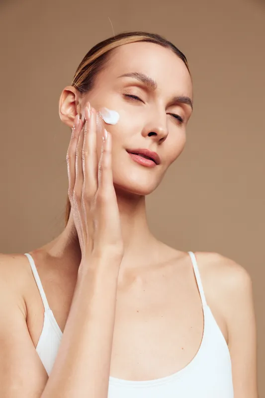 Calm woman applying cream to her face, closeup portrait, soft lighting, smooth skin, gentle expression, skincare routine, clear complexion, pampering moment, light makeup, natural look, relaxed