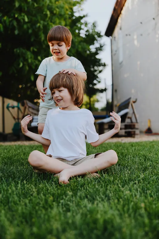 Playful boys enjoying a sunny afternoon in the garden, showcasing laughter and joy while sitting on the grass amidst a natural setting.