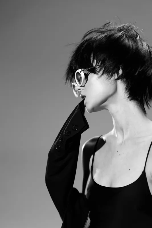 Black and white portrait of a stylish woman with short hair wearing sunglasses and a black top, expressing modern minimalistic fashion and elegance.