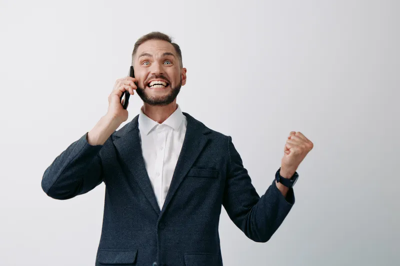 A professional man on a phone, in a blazer, shows confident, excited mood. Isolated colored background concept highlighting business success, leadership, and positive emotion in a clean studio shot.