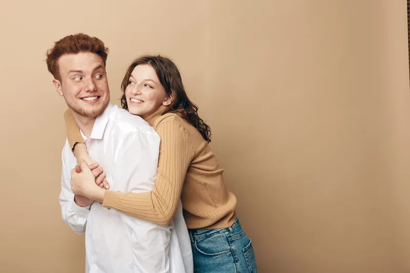 Happy young couple in casual clothes smiling and hugging each other against beige background. Concept of love, friendship, relationship, and positive emotions between people.