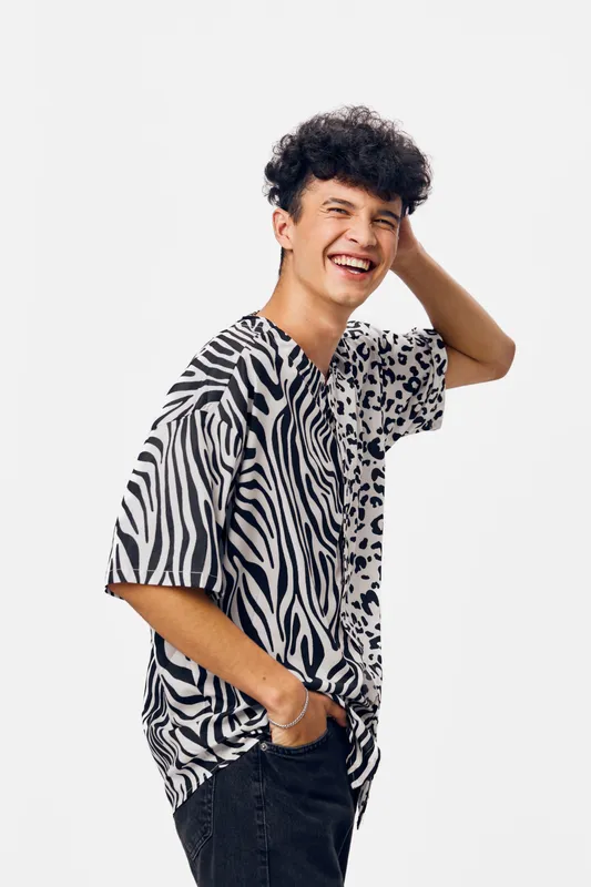 Smiling man wearing a black and white zebra print shirt stands against a white background with casual pose and joyful expression, embodying youthful energy and style.