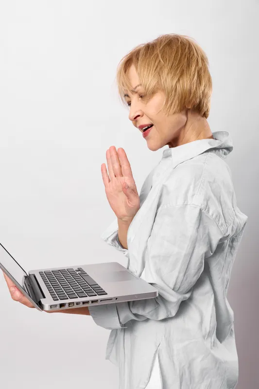 Woman laptop stressed warning communication healthcare doctor coat hand refusal, blonde senior in white coat holds laptop, raises hand to stop, worried background