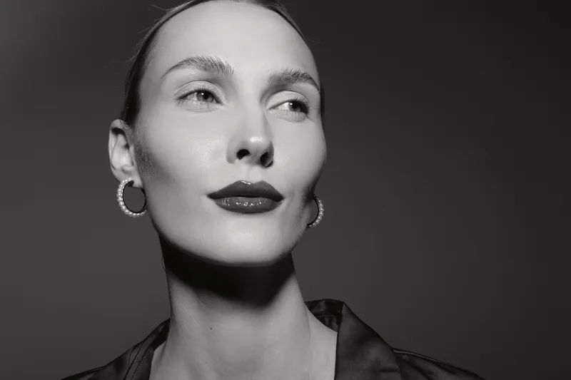 Elegant white woman with pale skin and slicked back hair wears hoop earrings in monochrome portrait studio.