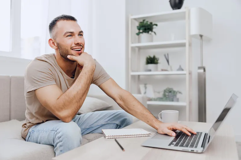 A thoughtful man sitting on a sofa, using a laptop and contemplating ideas. The cozy home setting encourages creativity and productivity in modern lifestyle.
