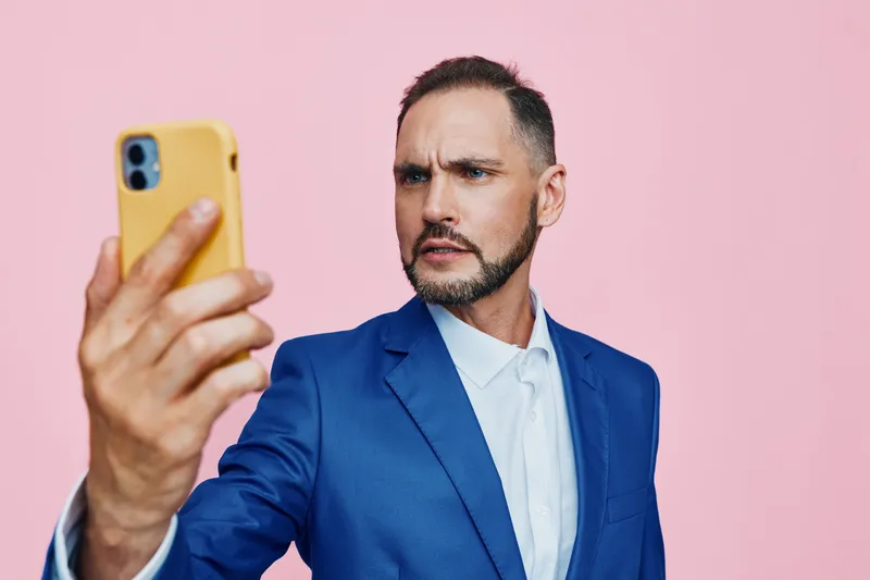 A professional man in a blue suit stands against an isolated pink background, conveying focus, confidence, and ambition in a confident self portrait style.