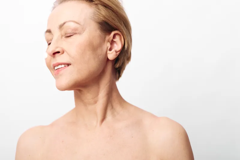 Mature woman with short hair smiles gently with closed eyes against white background. Concept of natural beauty, aging gracefully, self-acceptance and skin care at any age.