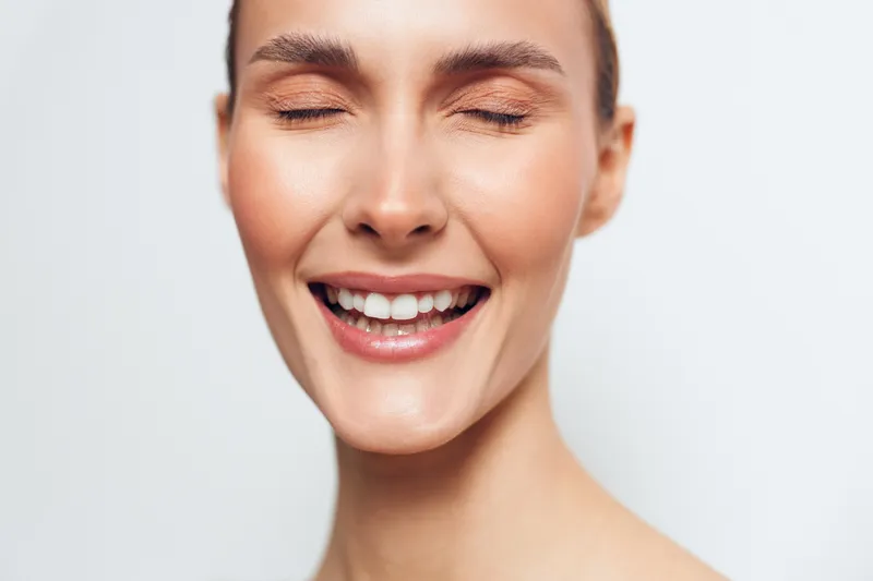 Woman face closeup smile shows fresh beauty and skincare, spa wellbeing concept, soft lighting on neutral background, natural makeup, confident cheerful mood, cosmetic care theme