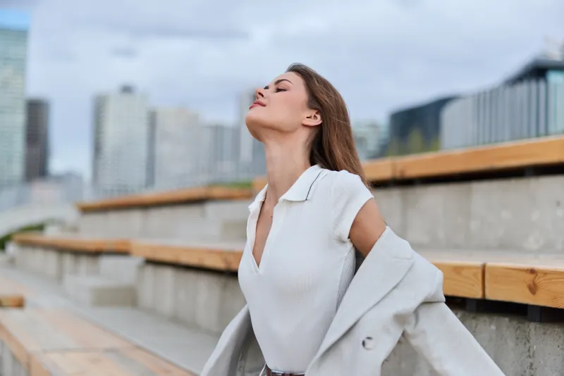 Young woman in white blouse feeling calm and confident outdoors urban background casual fashion style autumn season
