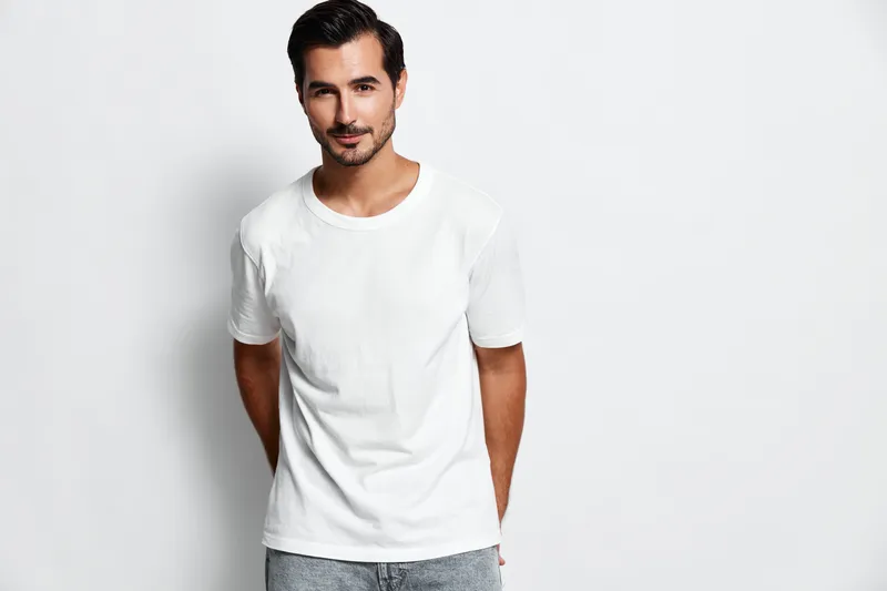 Handsome smiling young man wearing a white t-shirt poses confidently against a plain white background. Portrait concept featuring casual fashion style.