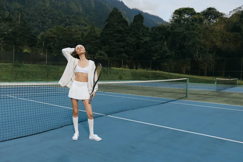 Young athletic woman in sporty outfit posing confidently on a tennis court, showcasing her passion for sport, fitness, and a healthy lifestyle