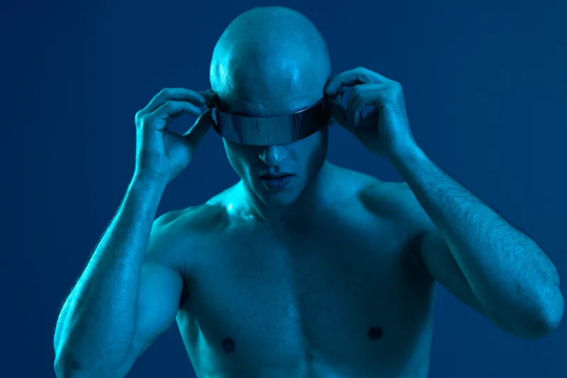 Futuristic man adjusting stylish visor, showcasing a bold, modern look. The image features a captivating blue light, enhancing the sleek atmosphere.