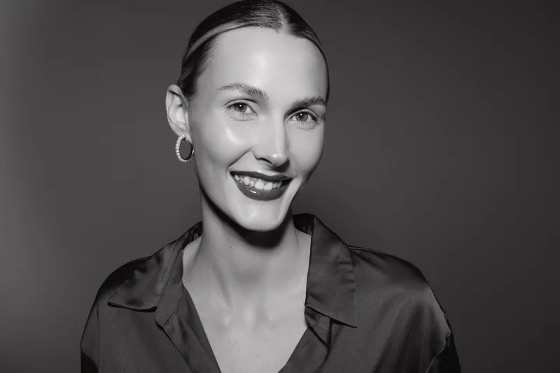 Smiling caucasian woman with fair skin and slicked back hair wears dark blouse and hoop earrings in black and white studio portrait. Concept of elegance, beauty, and fashion.