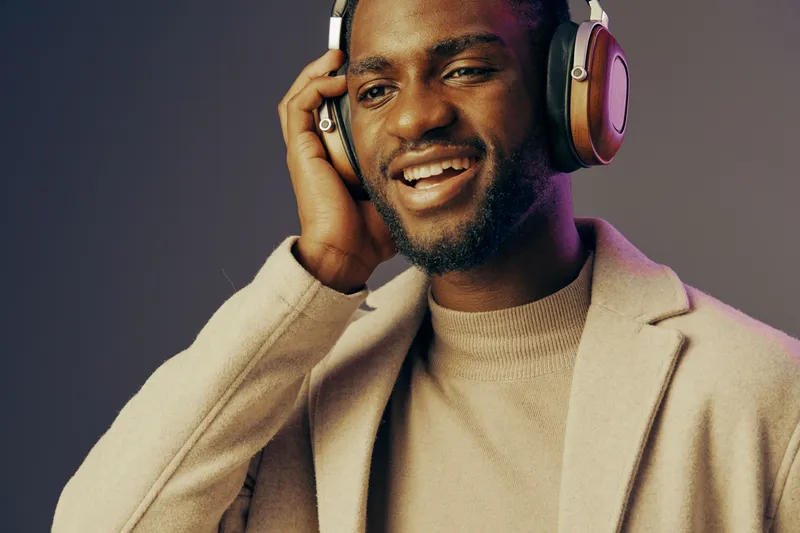 Young African man smiling with headphones, enjoying music in a stylish beige outfit against a soft gradient background, perfect for lifestyle and technology concepts